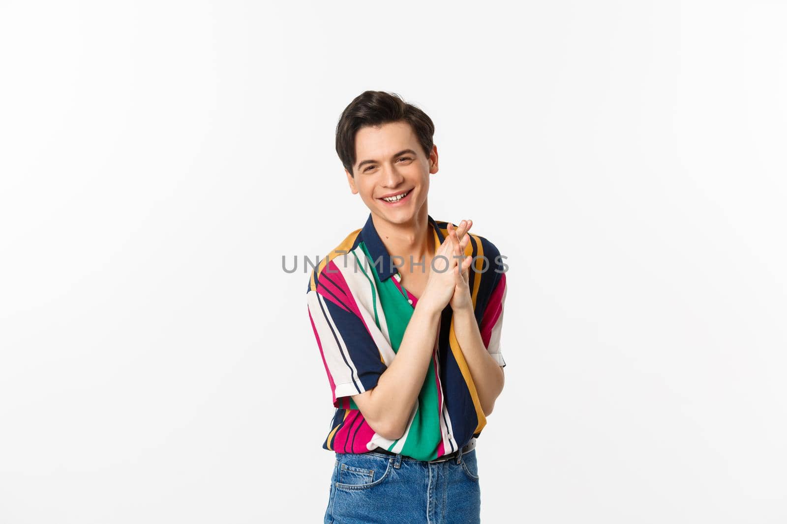 Attractive young slim man relish something good, rubbing hands and smiling satisfied, standing over white background. Copy space
