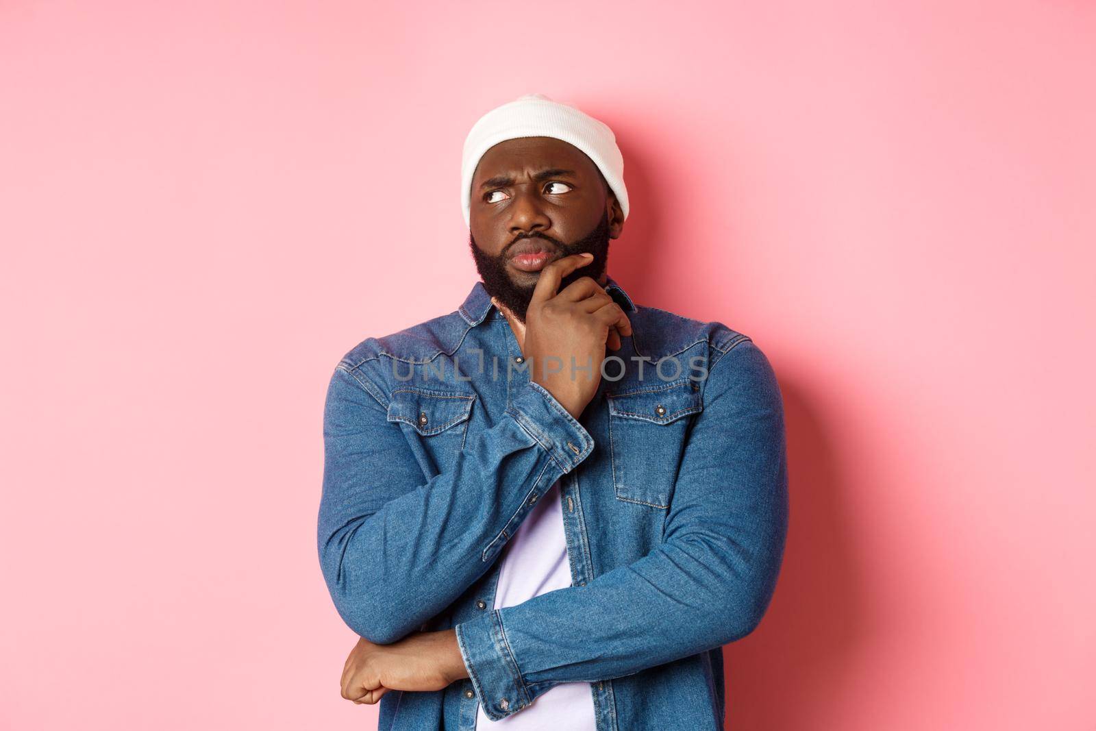 Doubtful african american man staring at upper left corner thoughtful, making decision and thinking, standing over pink background.