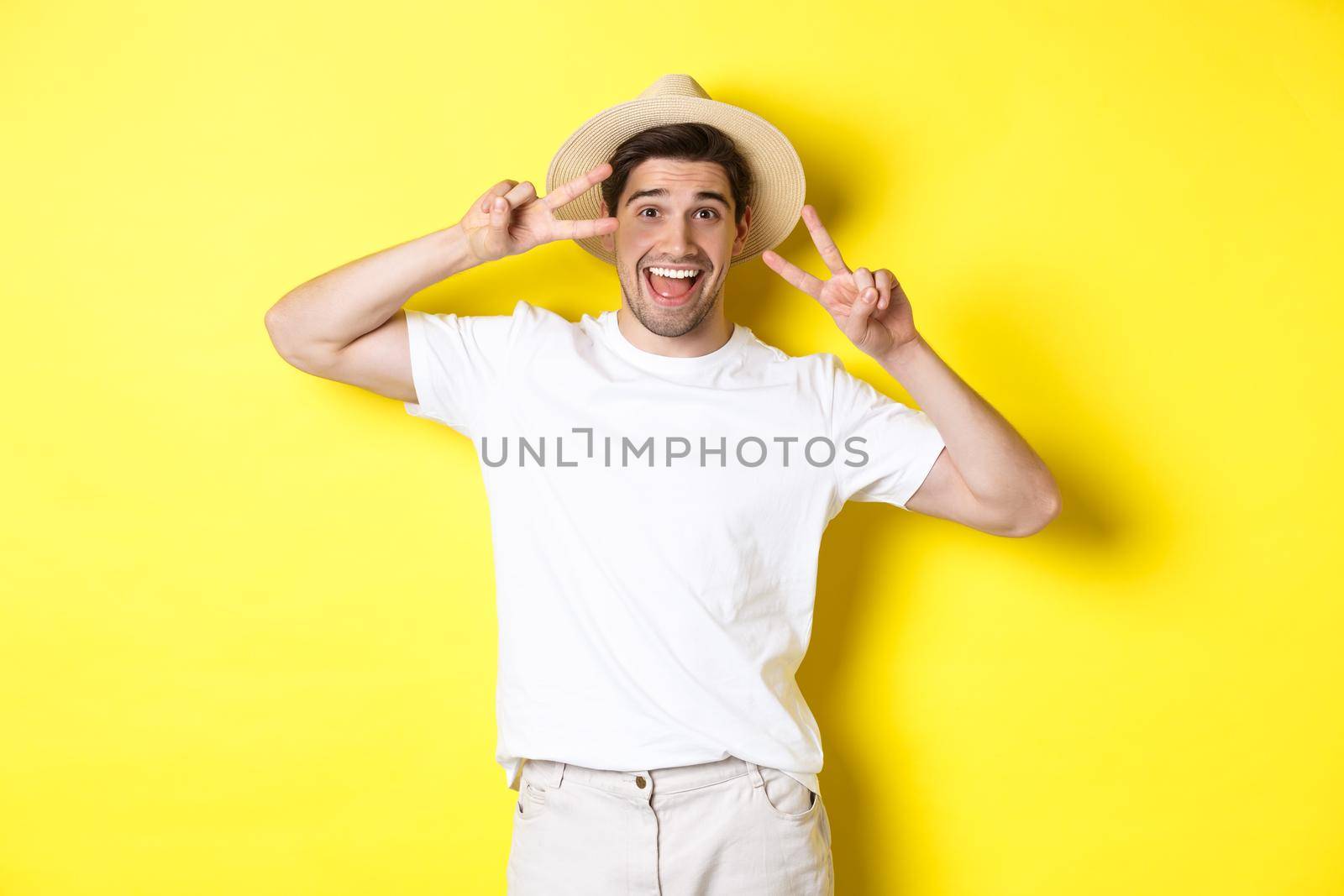 Concept of tourism and vacation. Happy man tourist posing for photo with peace signs, smiling excited, standing against yellow background by Benzoix