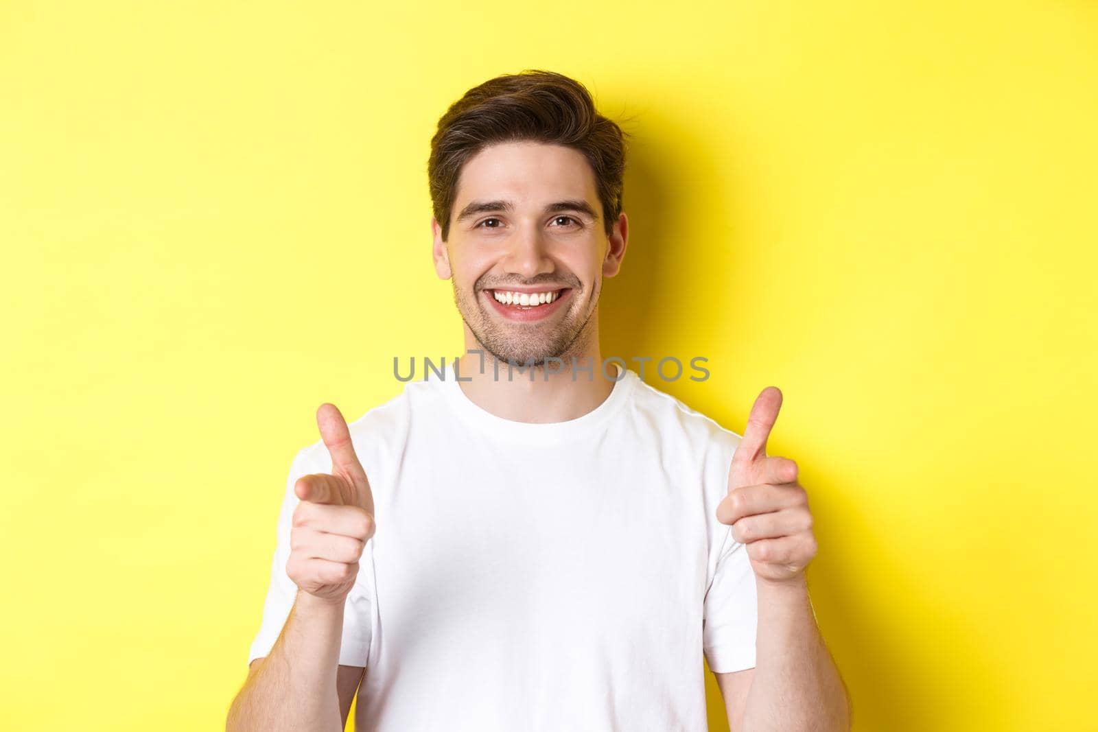 Confident man pointing fingers at camera and smiling, praising you, standing over yellow background by Benzoix
