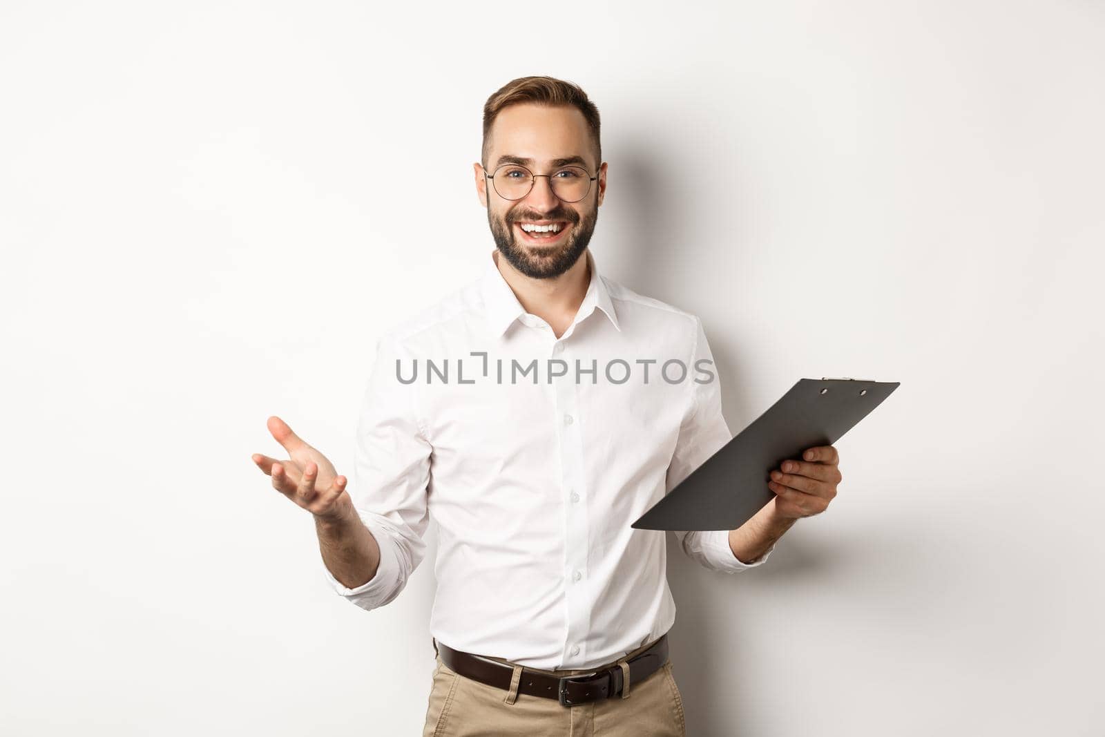 Handsome boss looking satisfied, holding clipboard and praising you, standing over white background.