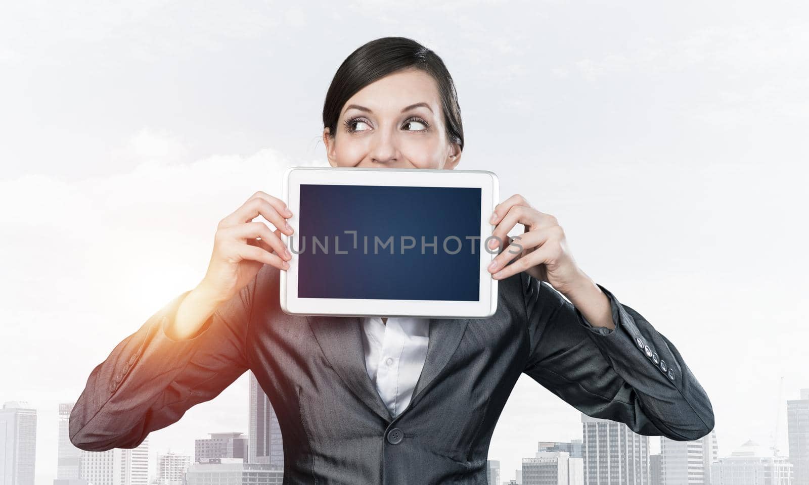 Businesswoman holding tablet computer with blank screen. Beautiful woman in business suit show tablet PC near her face. Corporate businessperson on cityscape background. Digital technology layout.