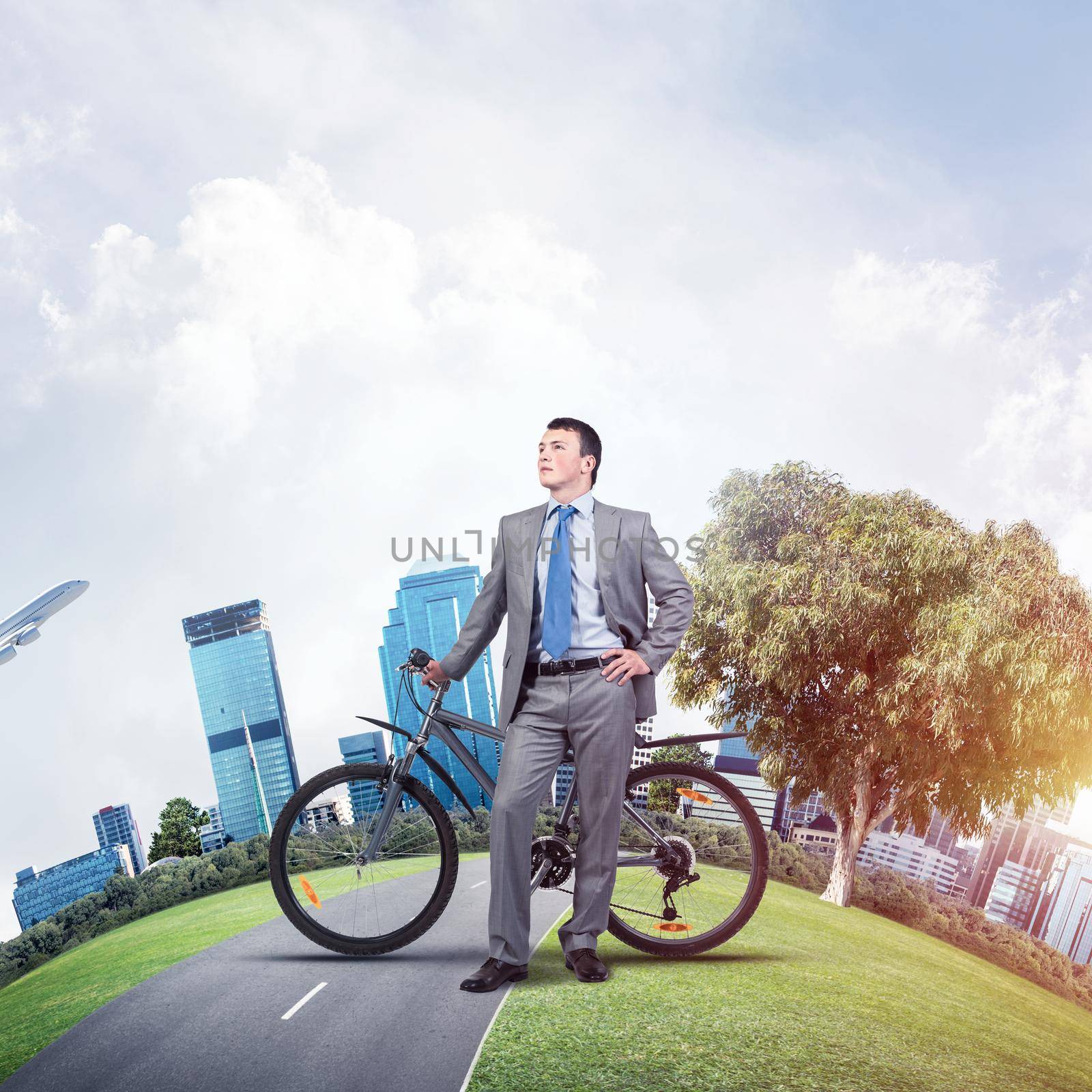 Young man wearing business suit and tie standing on asphalt road with bike. Businessman with bicycle on background world round panorama of modern megalopolis. Handsome cyclist relaxing outdoors.