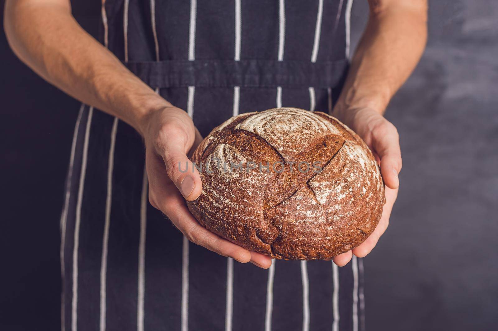 Baker man holding homemade rustic wheat bread in hands. Selective focus.