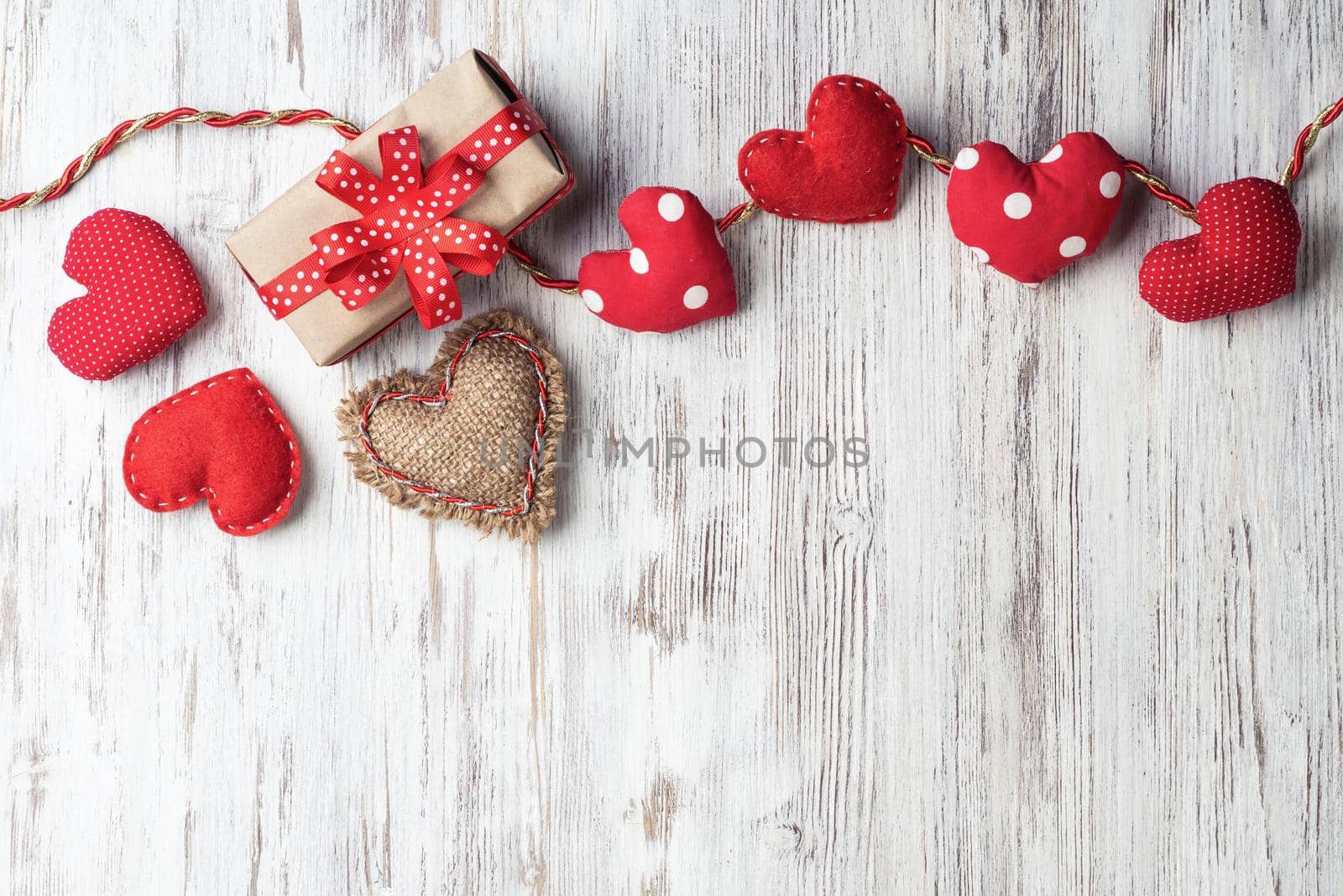 Flat lay cute composition with handmade fabric red hearts. Gift box with ribbon bow on wooden table. Happy birthday or anniversary congratulation. Romantic message template with copy space.