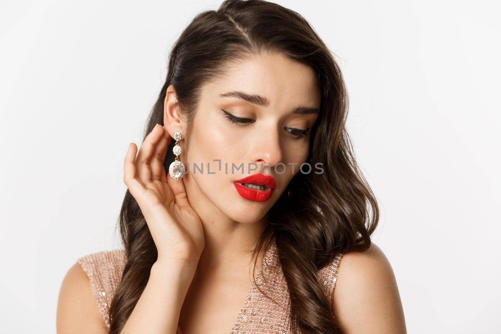 Concept of New Year celebration and winter holidays. Headshot of elegant brunette woman with red lips, showing earrings and looking sensual, white background.