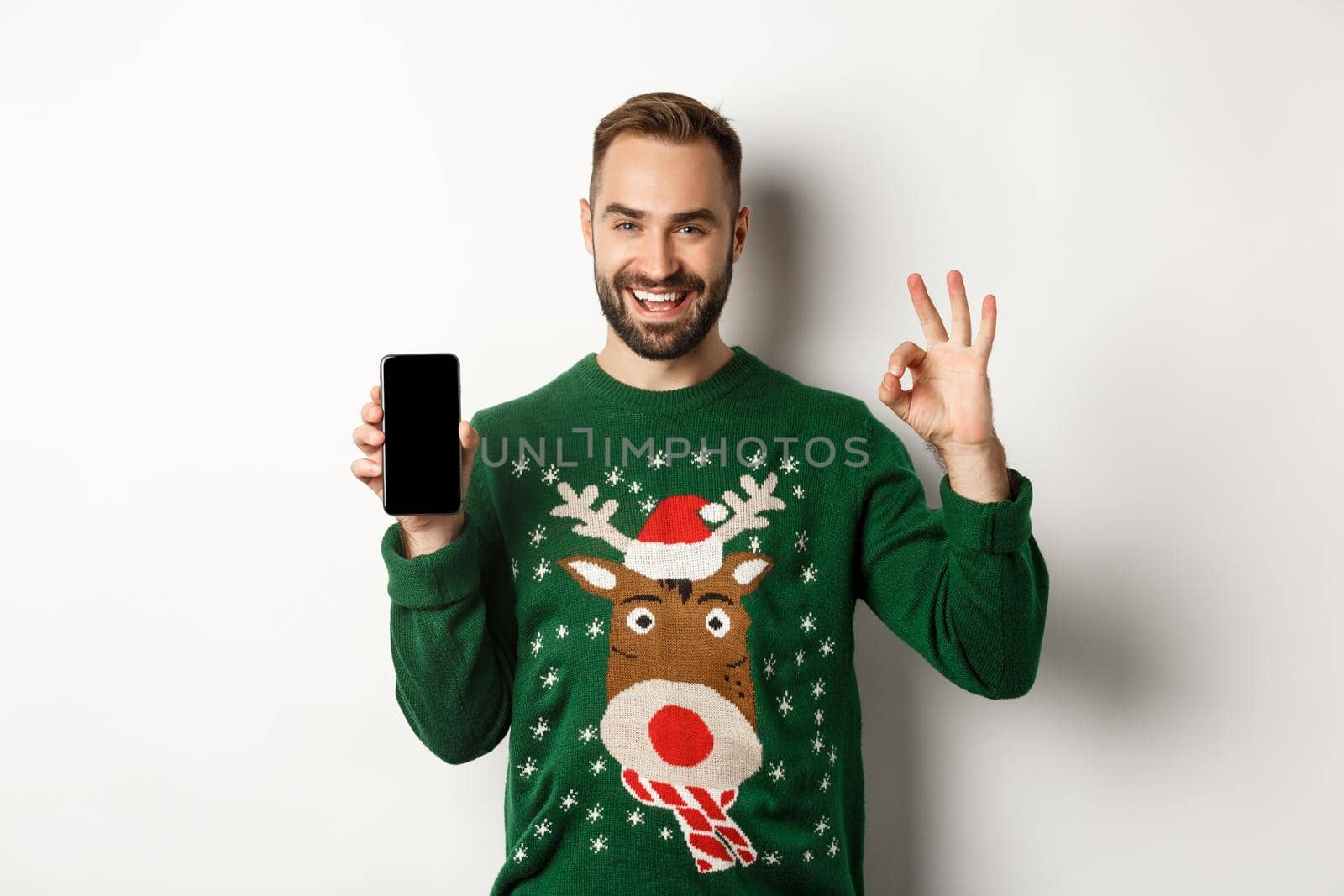 New Year, holidays and celebration. Satisfied young male buyer showing OK sign and mobile screen, recommending an app, standing over white background.