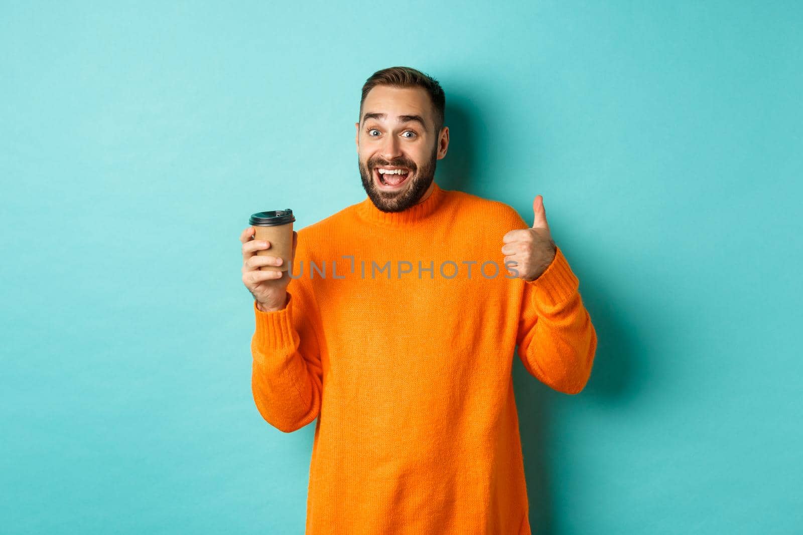 Handsome satisfied man showing thumbs-up, like coffee, smiling pleased, standing over turquoise background. Copy space