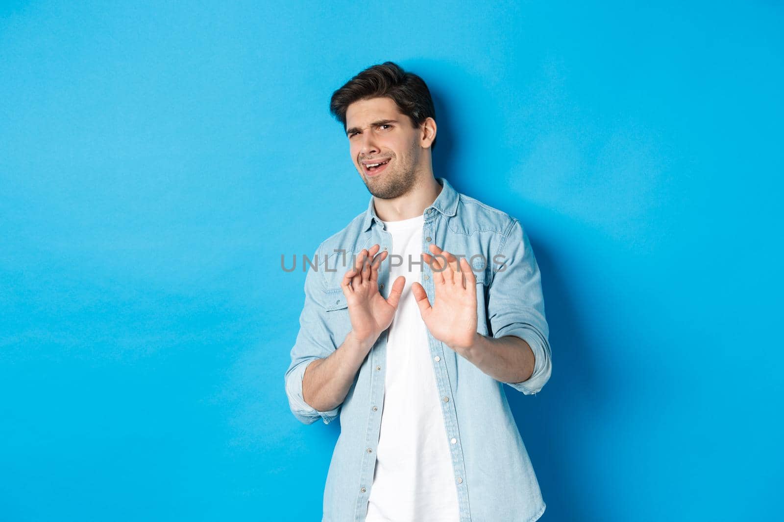 Displeased man refusing, saying no and cringe from something disgusting, standing over blue background.
