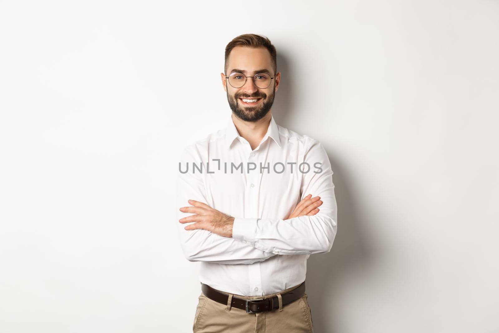 Business. Young professional businessman in glasses smiling at camera, cross arm on chest with confidence, standing over white background.