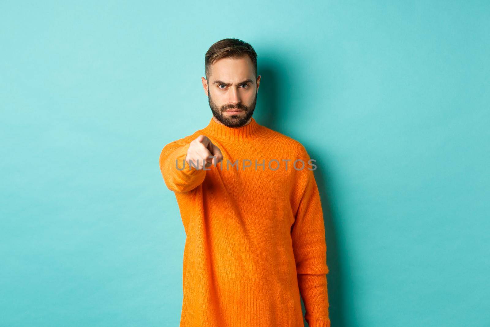 Confident man blame you, frowning and pointing finger at camera, accuse person, judgemental stare, standing over light blue background by Benzoix