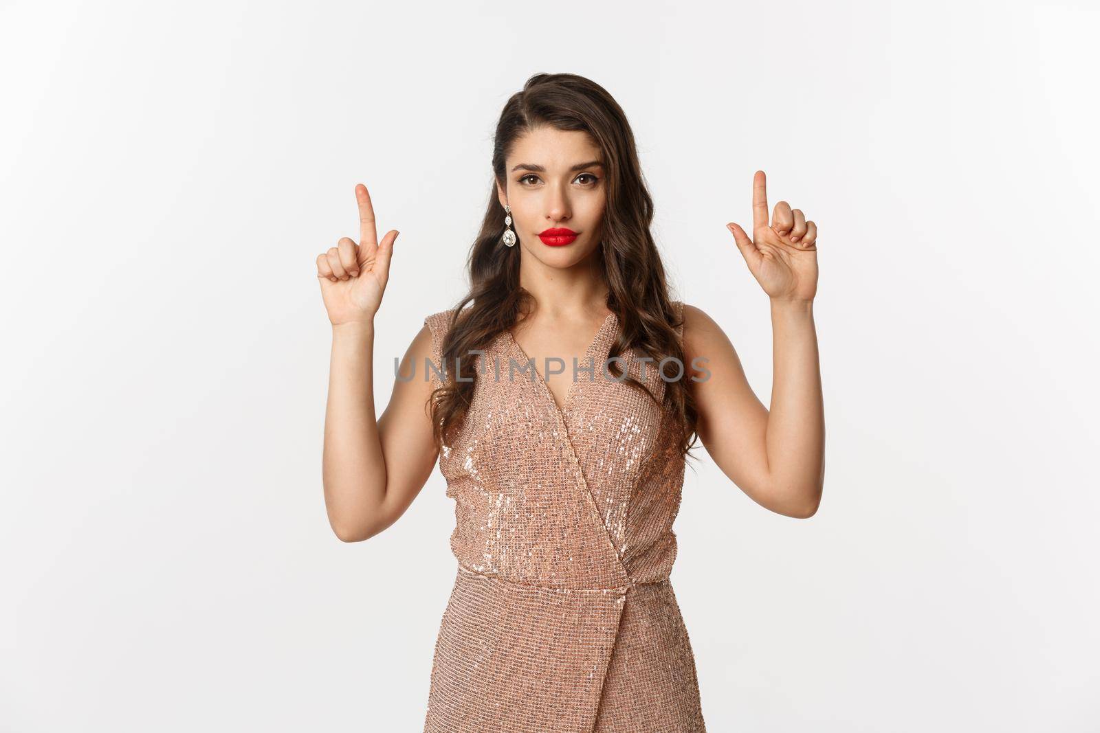 New Year, christmas and celebration concept. Elegant young woman with red lipstick, wearing party dress and looking sassy, pointing fingers up at logo, white background.