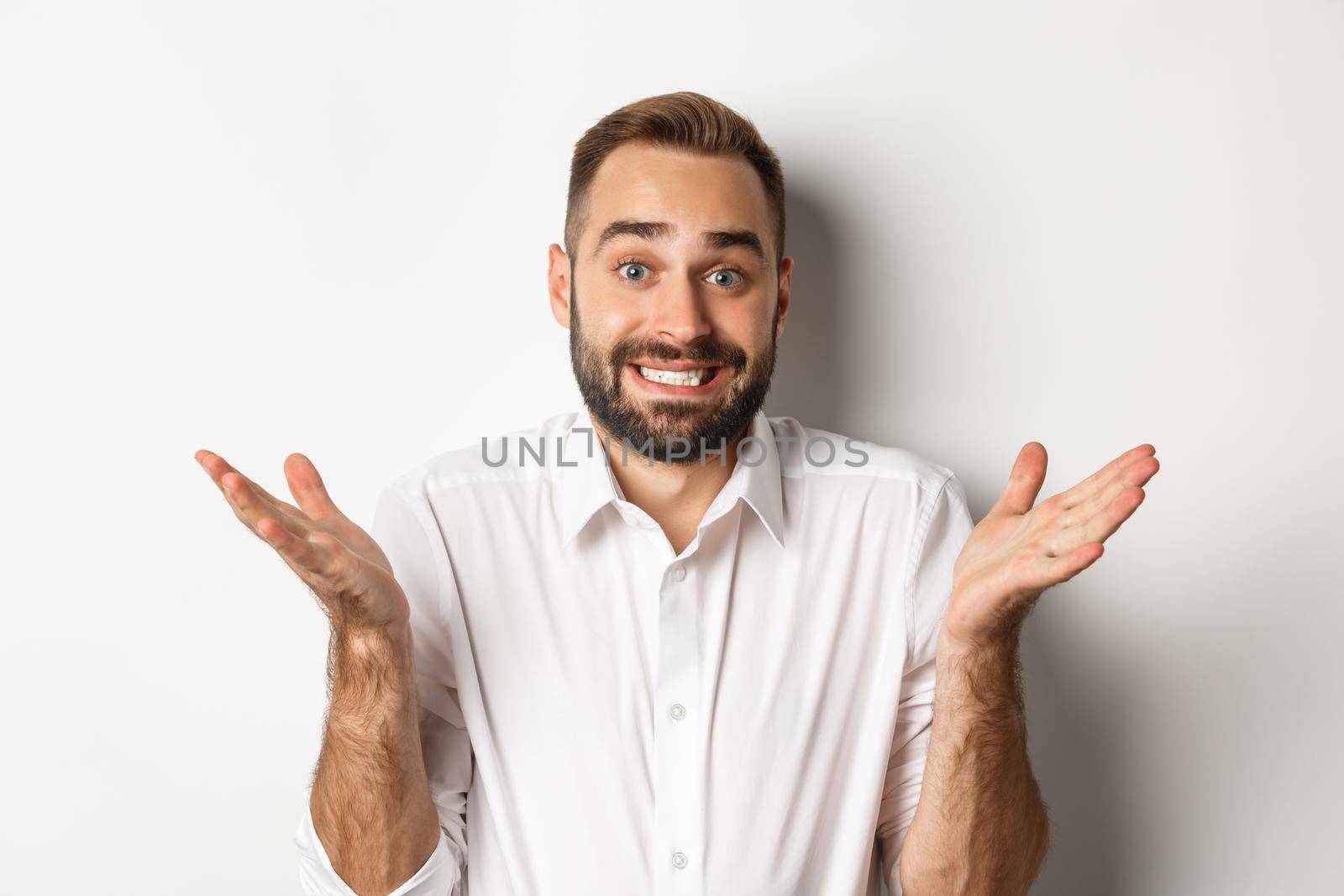 Close-up of awkward manager shrugging and smiling with sorry look, standing clueless over white background.