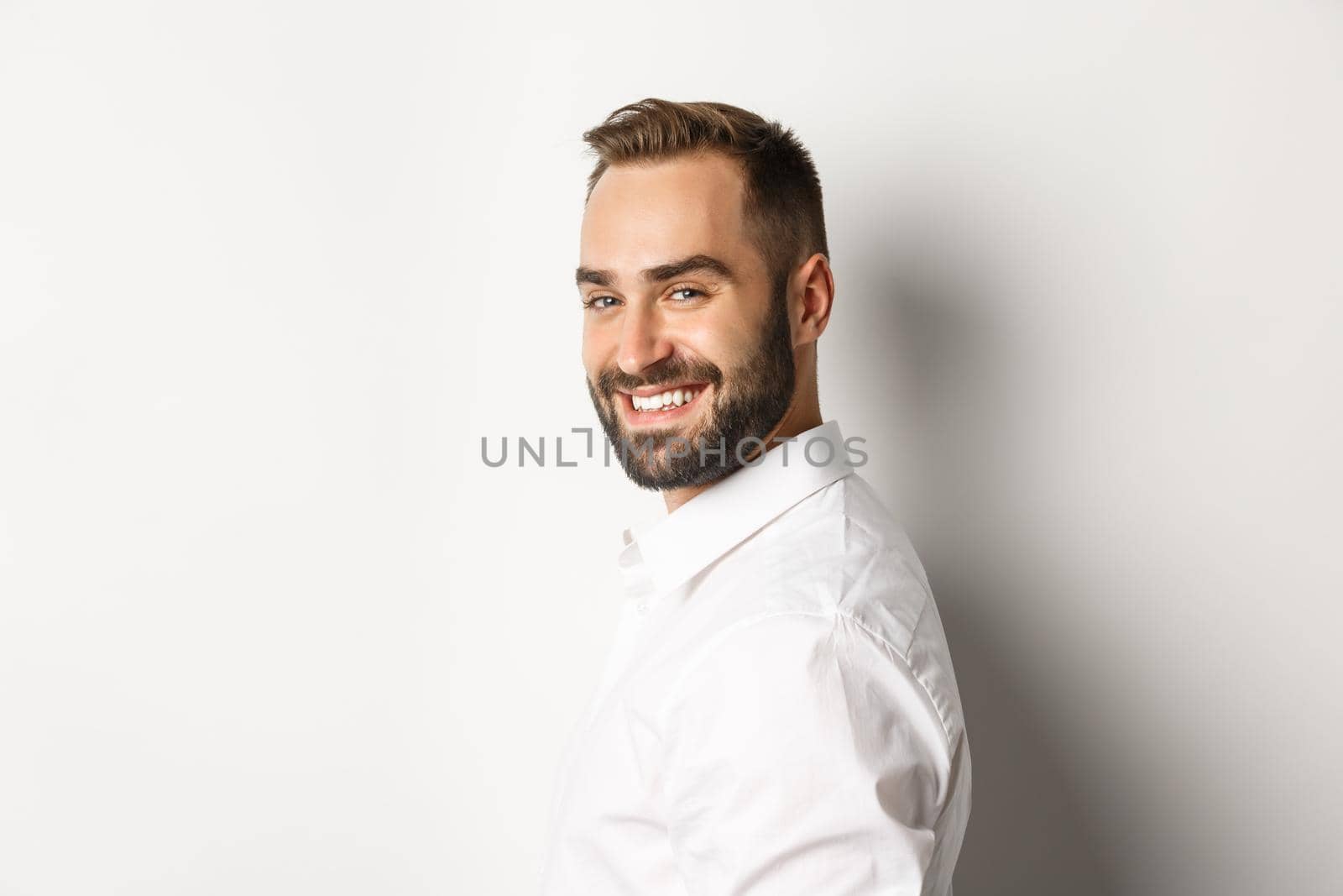 Close-up of confident businessman turn face at camera, smiling self-assured, standing over white background.
