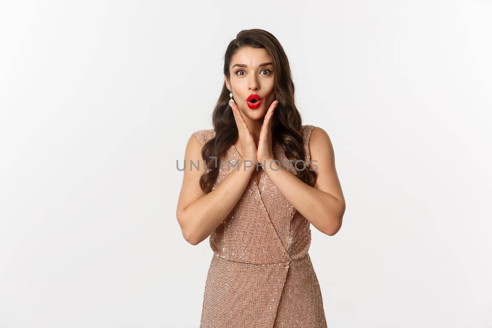 Celebration and Christmas. Attractive young woman looking surprised at New Year gift, wearing evening dress for party, stare at camera amazed, standing over white background.