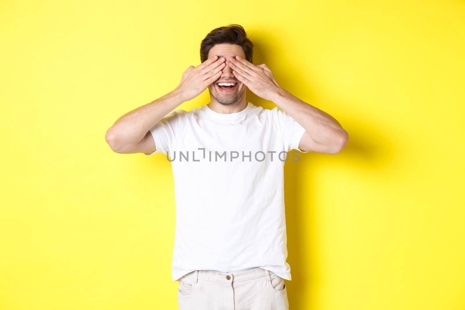 Happy man close eyes and waiting for surprise, smiling amused, standing over yellow background by Benzoix