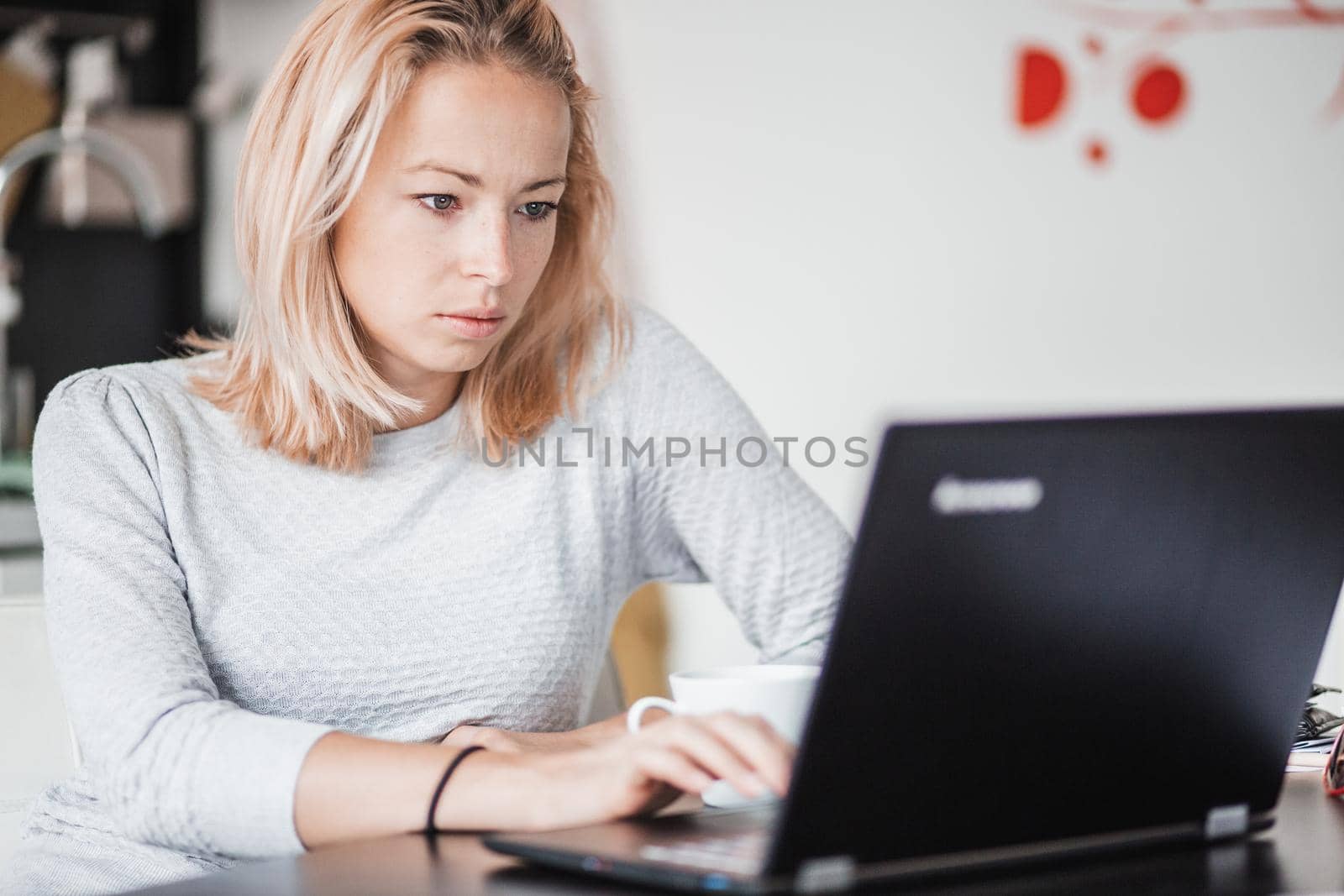 Female freelancer in her casual home clothing working remotly from her dining table in the morning. Home kitchen in the background