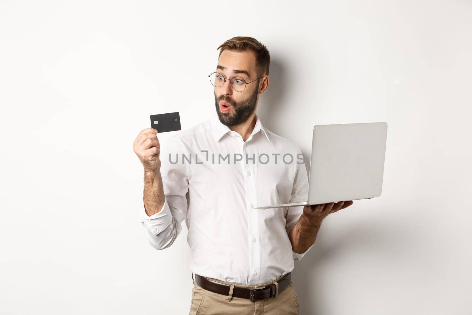Online shopping. Amazed businessman holding laptop, looking impressed at credit card, standing over white background.