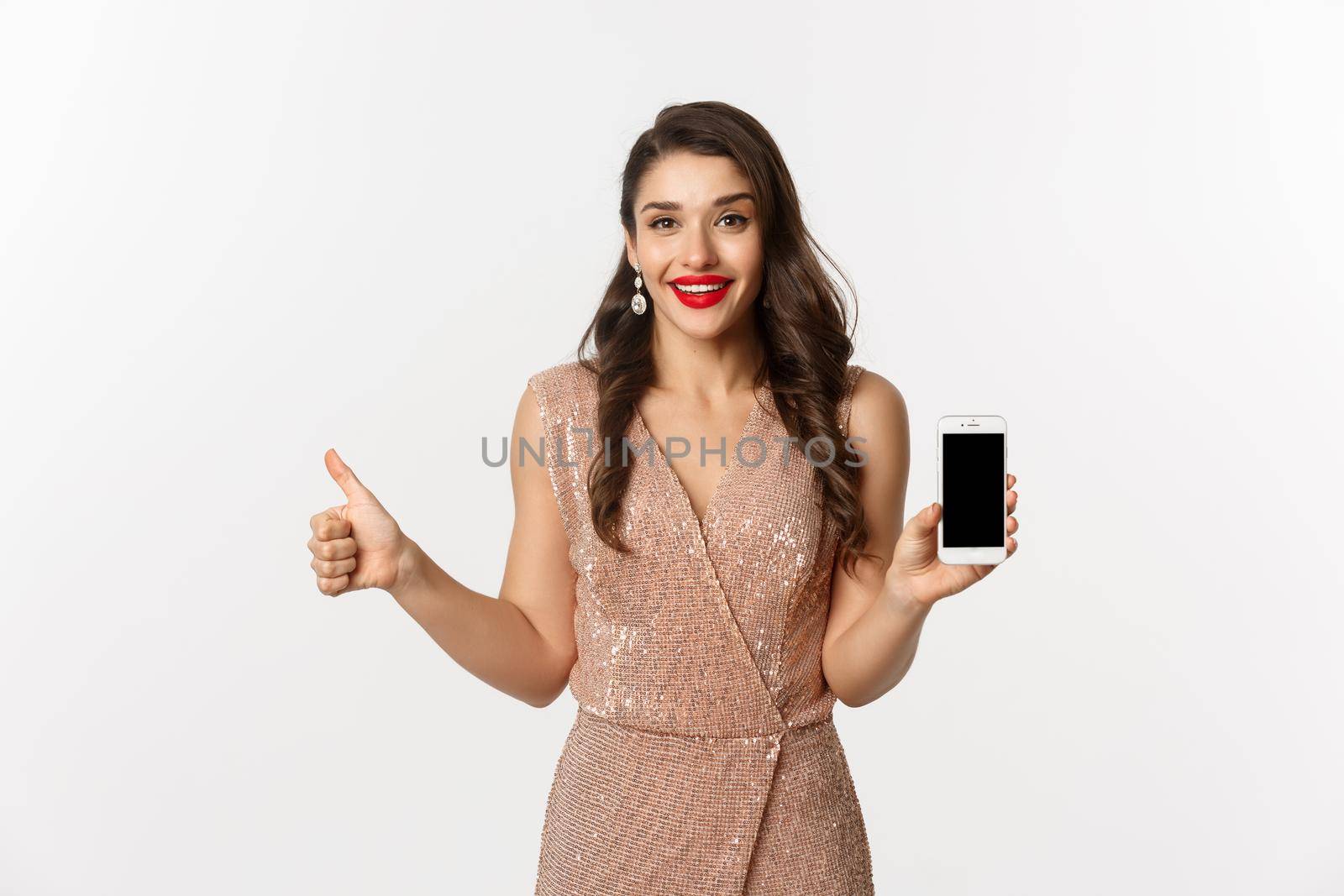 Online shopping. Beautiful young woman in party dress and makeup, showing thumbs up and mobile screen, praising good app, white background.