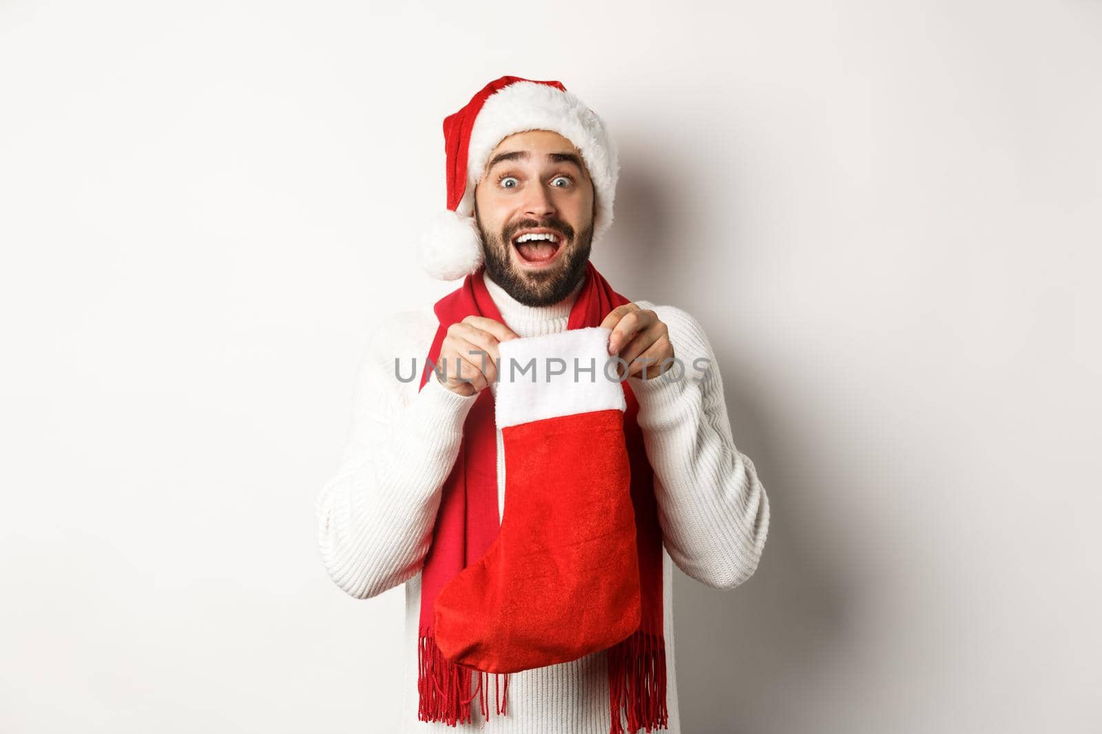 Winter holidays and celebration concept. Surprised bearded man looking inside Christmas sock, receiving New Year gift, standing over white background by Benzoix