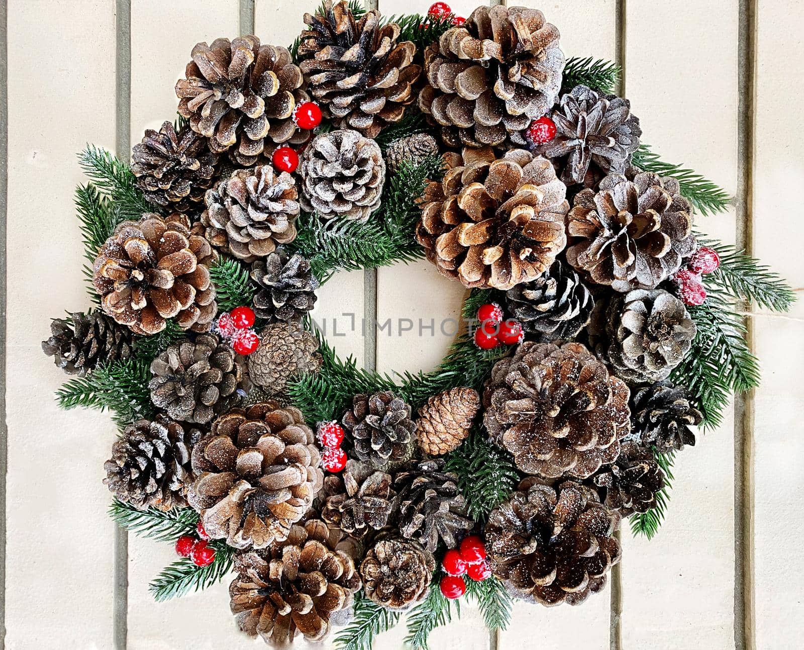 Christmas decorative wreath of ivy, mistletoe, cedar and deciduous twigs with pine cones on a white brick wall background.