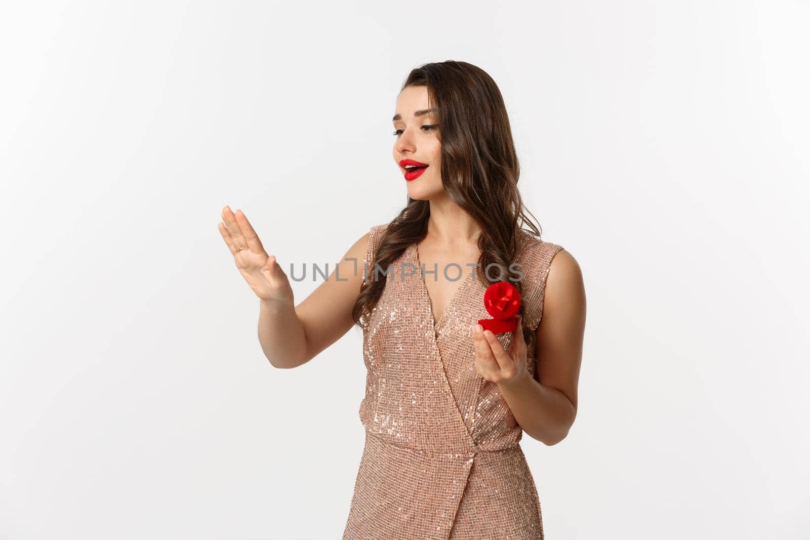 Beautiful woman in luxury dress, trying on engagement ring, saying yes to marriage proposal, looking dreamy at hand, standing over white background.