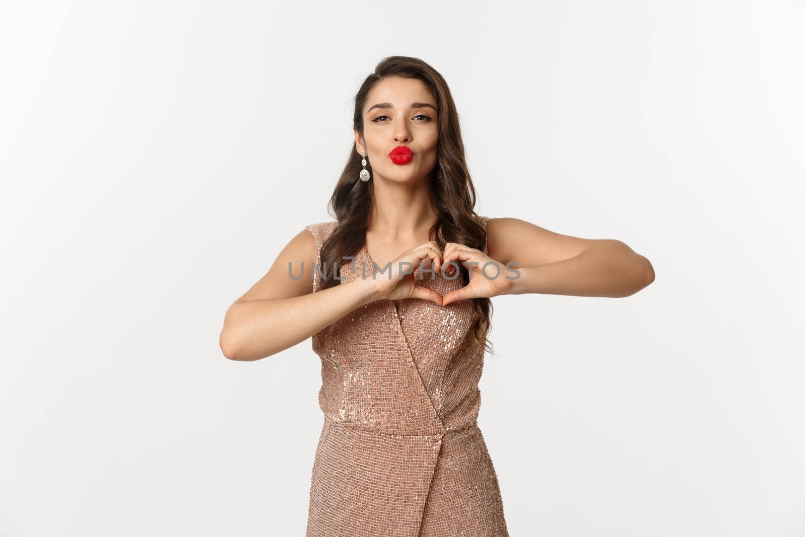 Celebration and party concept. Beautiful young woman in stylish dress, red lips, showing heart sign and waiting for kiss, standing over white background by Benzoix