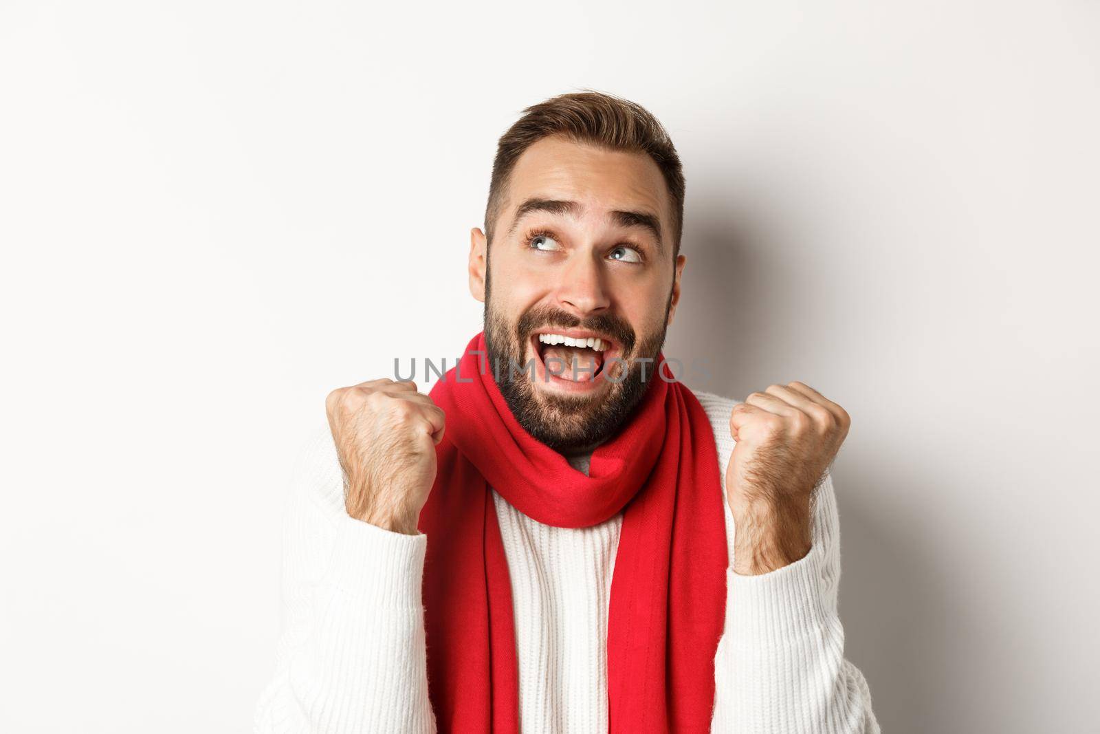 Christmas holidays. Close up of handsome man feeling excited about New Year party, fist pump and looking up amazed, white background by Benzoix