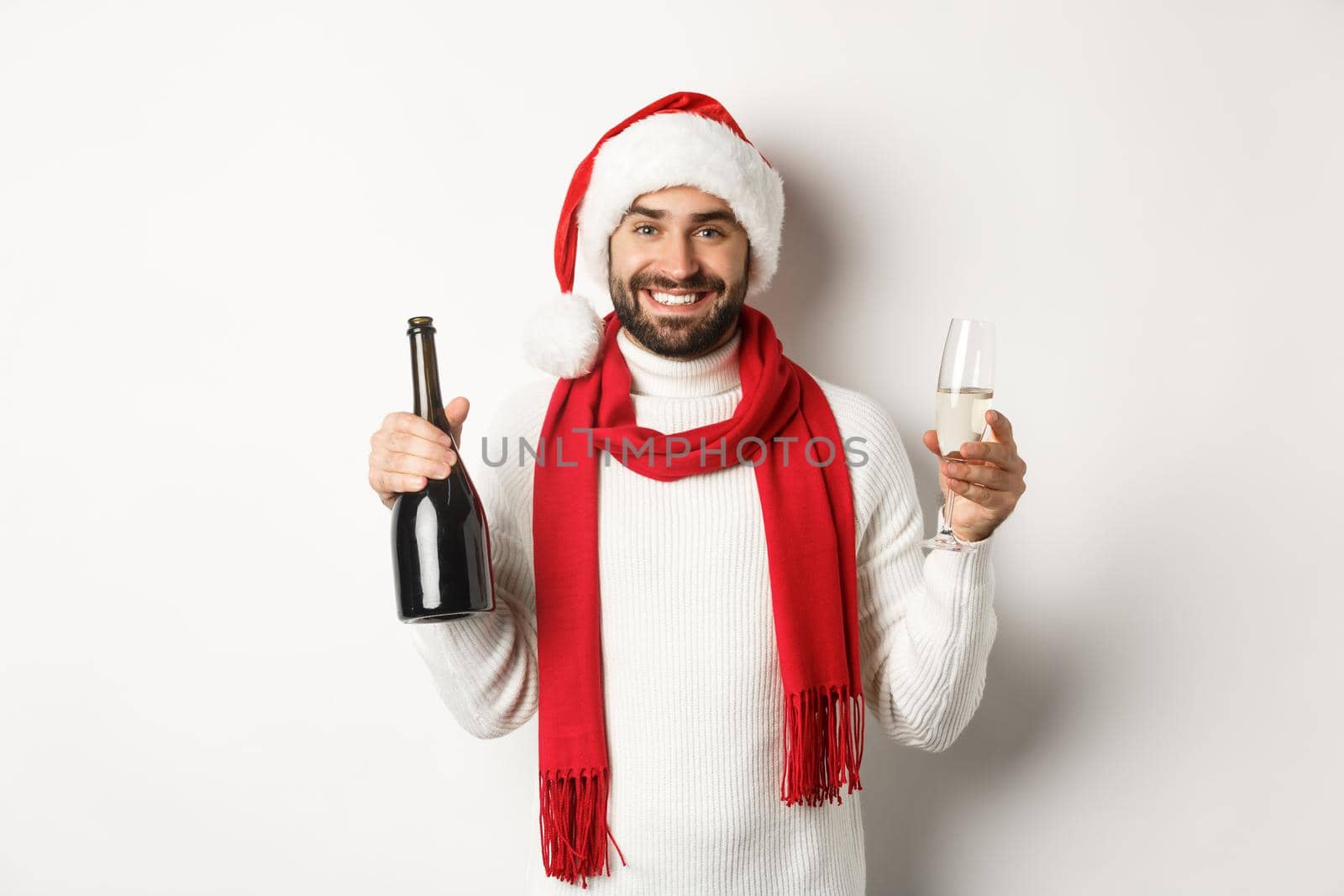 Christmas party and holidays concept. Happy bearded man in Santa hat, celebrating New Year, drinking champagne, standing over white background by Benzoix