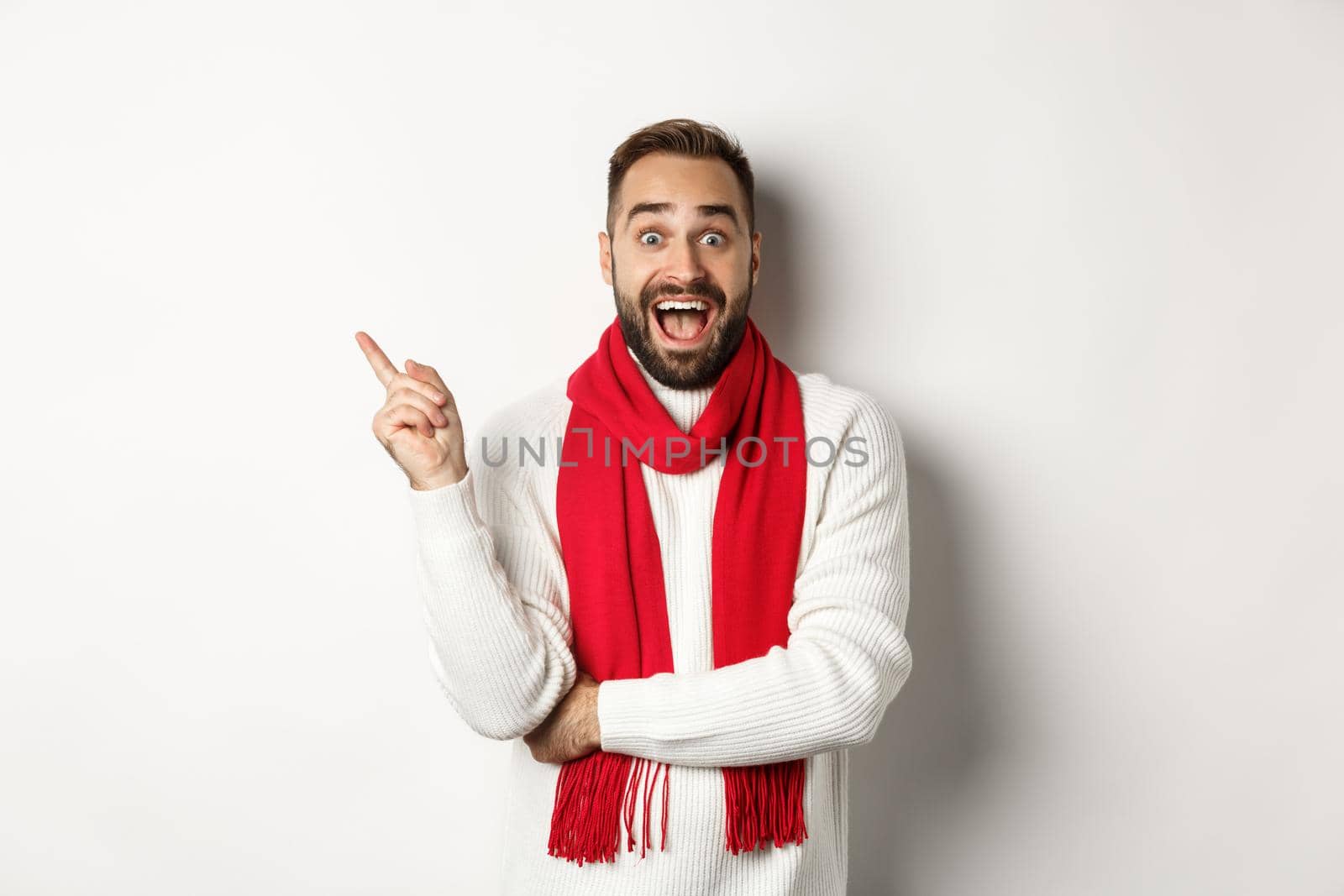 Christmas shopping and winter holidays concept. Surprised man pointing finger left, showing promo offer, standing over white background.