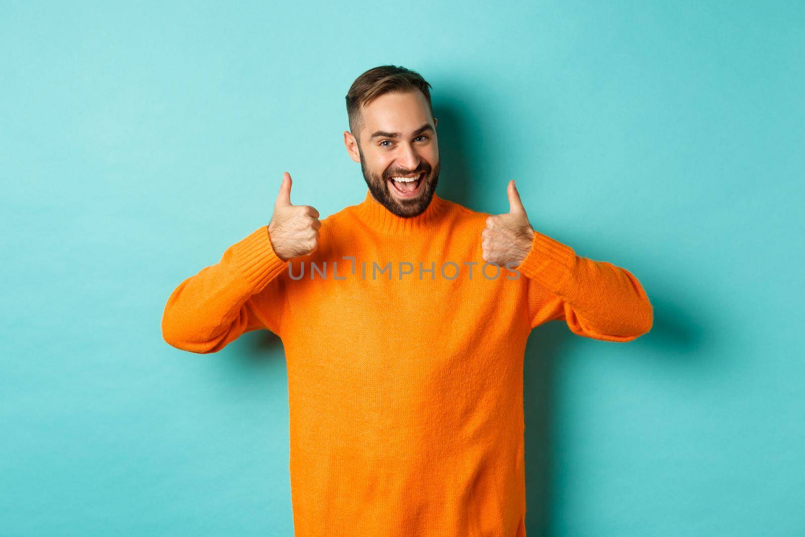 Handsome man expressing support, showing thumb up, encourage you, praise excellent work, approve and agree, standing over light blue background by Benzoix