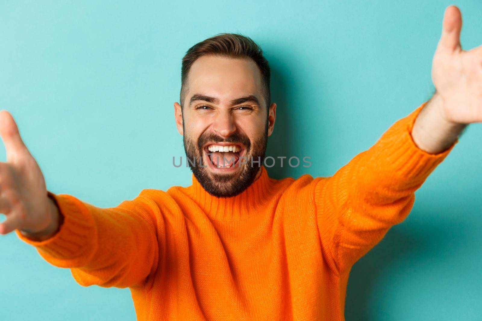 Close-up of handsome happy man reaching hands forward, stretching arms for hug, standing against turquoise background by Benzoix