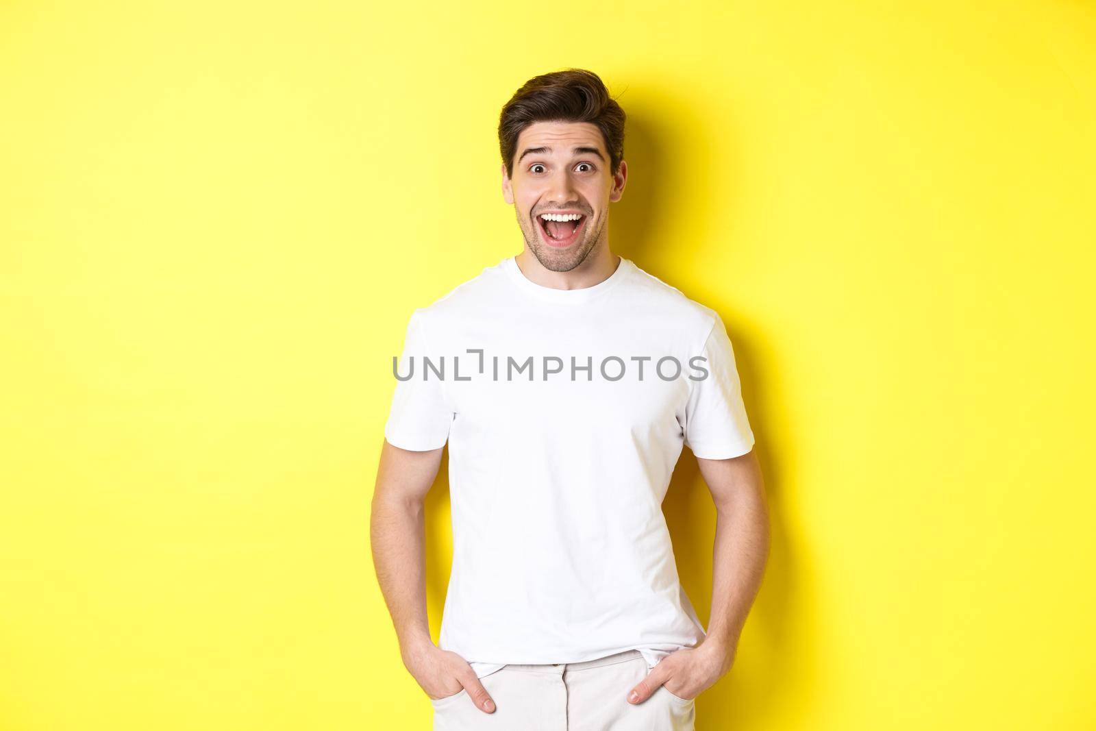 Man looking surprised, smiling amazed and looking at announcement, standing near copy space, yellow background.