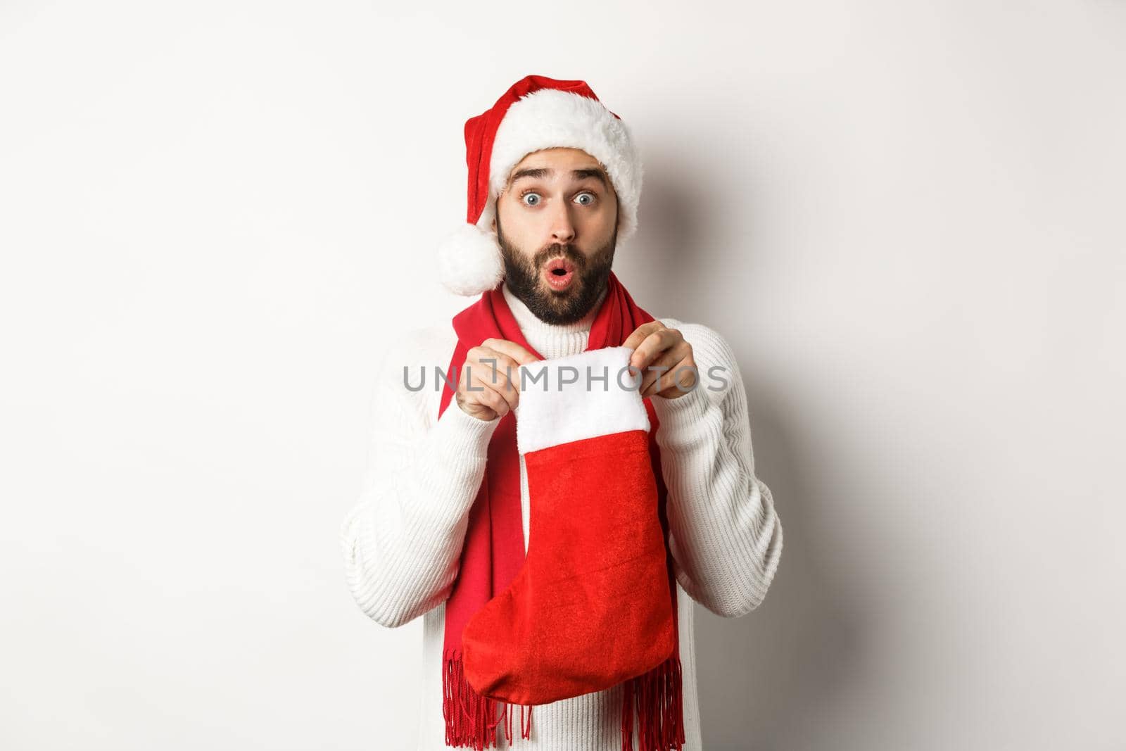 Winter holidays and celebration concept. Surprised bearded man looking inside Christmas sock, receiving New Year gift, standing over white background.