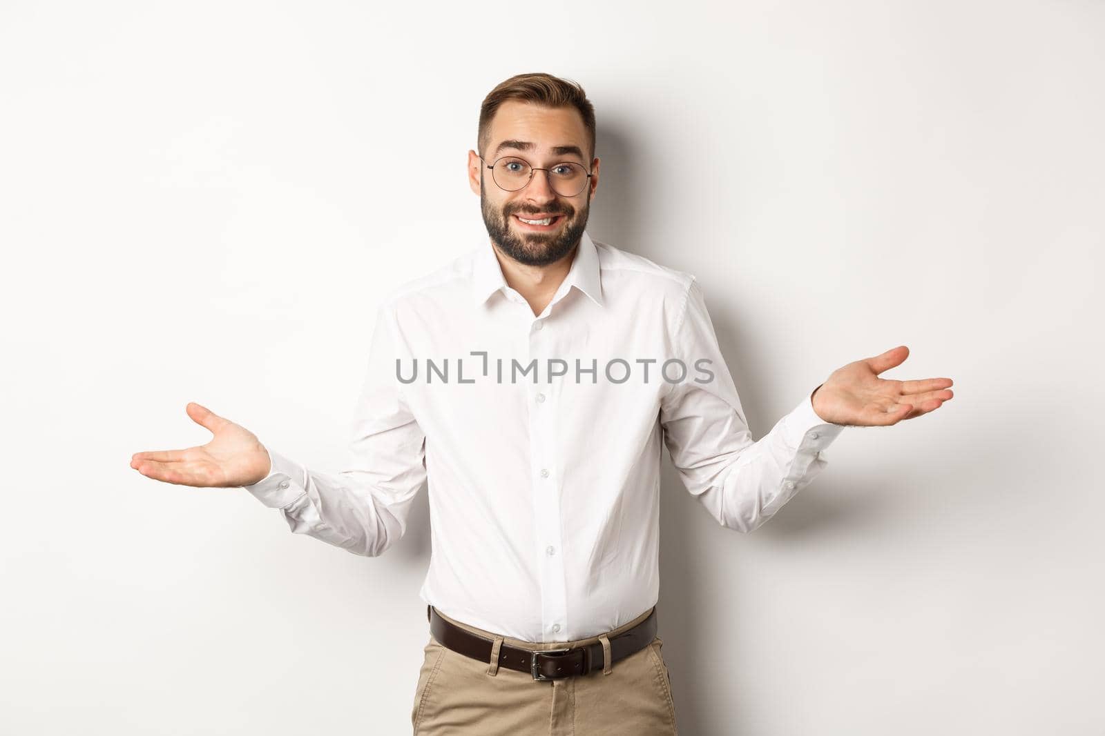 Confused smiling businessman dont know, shrugging and saying sorry, standing over white background by Benzoix