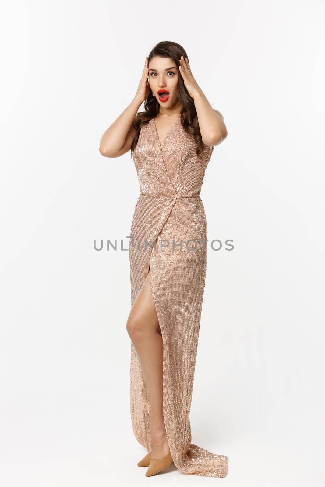 Christmas party and celebration concept. Full length of beautiful brunette woman looking surprised, wearing elegant dressed and staring with disbelief at camera, white background.