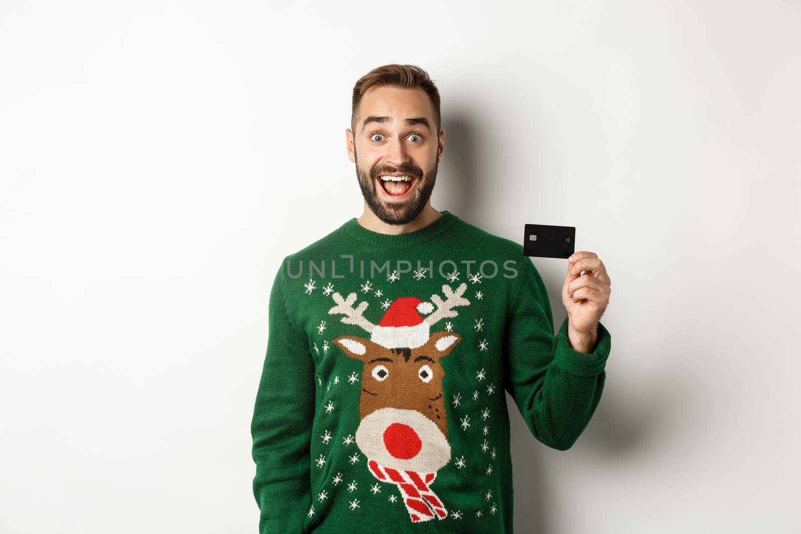 Christmas holidays and shopping concept. Cheerful man showing credit card, standing over white background.