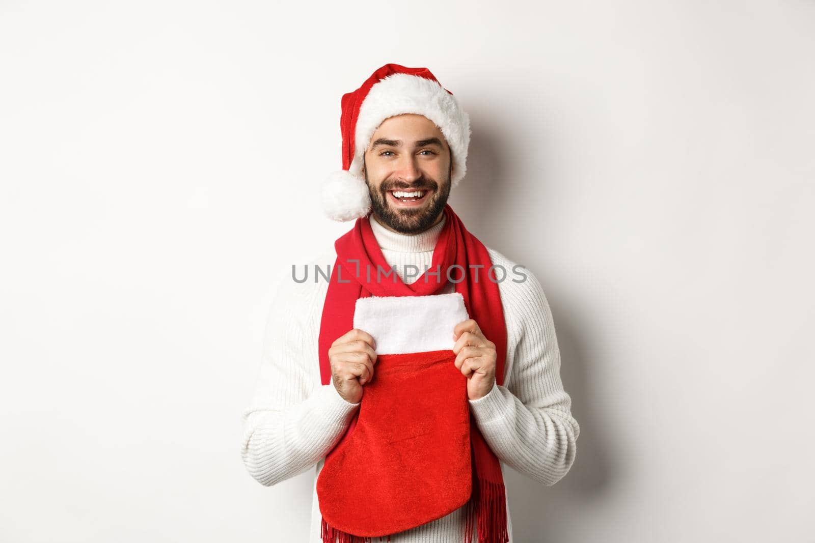 Winter holidays and shopping concept. Handsome bearded man bring presents in Christmas sock, smiling and wishing happy New Year, white background.