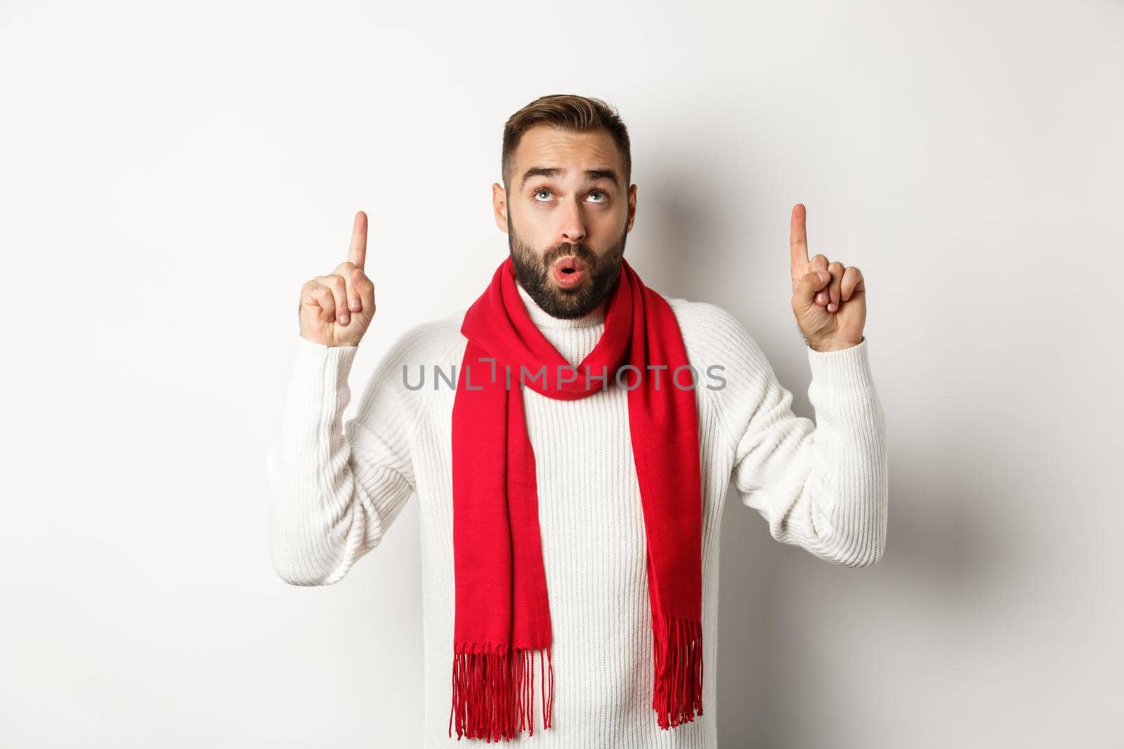 Christmas shopping and winter holidays concept. Amazed bearded man checking out new year promo offer, pointing and looking up, standing against white background.