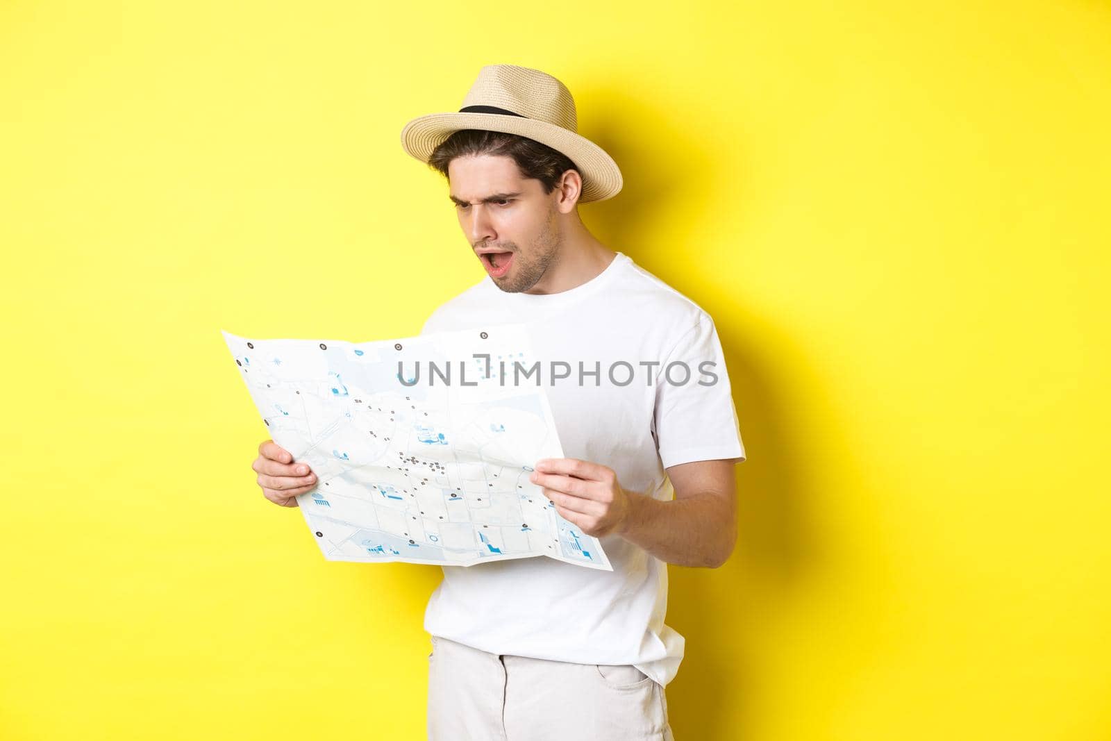 Travelling, vacation and tourism concept. Tourist looking displeased and shocked at road map, standing against yellow background by Benzoix