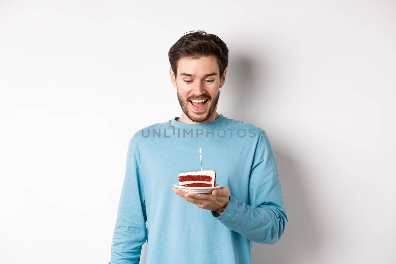 Cheerful man looking happy at birthday cake, celebrating bday, standing over white background.