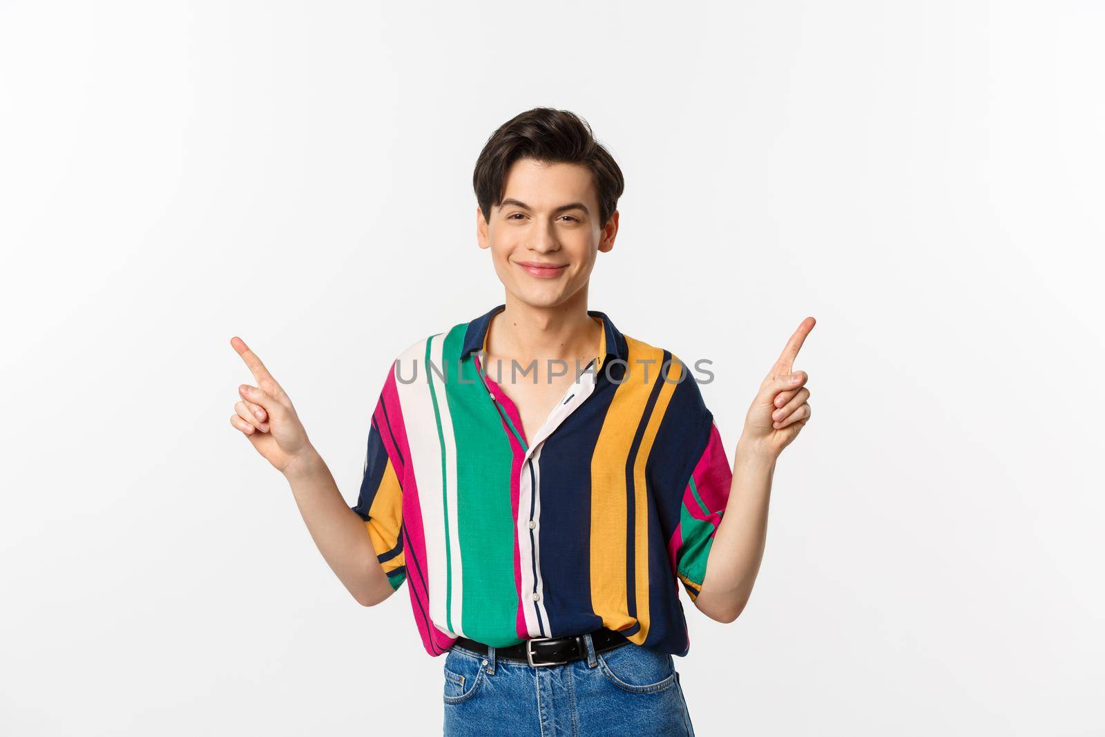Handsome queer man pointing fingers sideways, smiling pleased and showing two choices, standing over white background by Benzoix