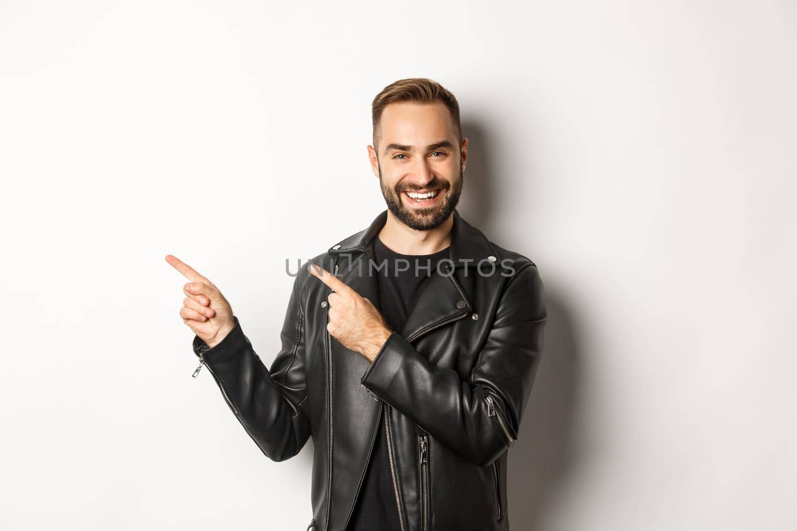 Confident macho man in black leather jacket, pointing fingers left at promo offer, showing logo, white background by Benzoix