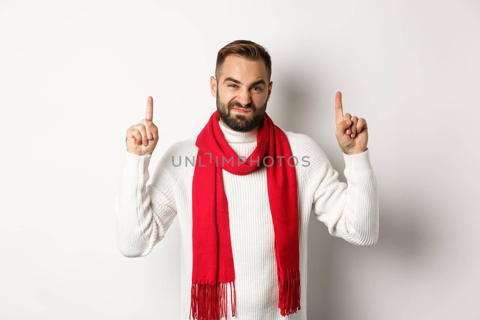 Christmas shopping and winter holidays concept. Displeased and skeptical guy complaining, pointing fingers up at bad product, standing against white background by Benzoix