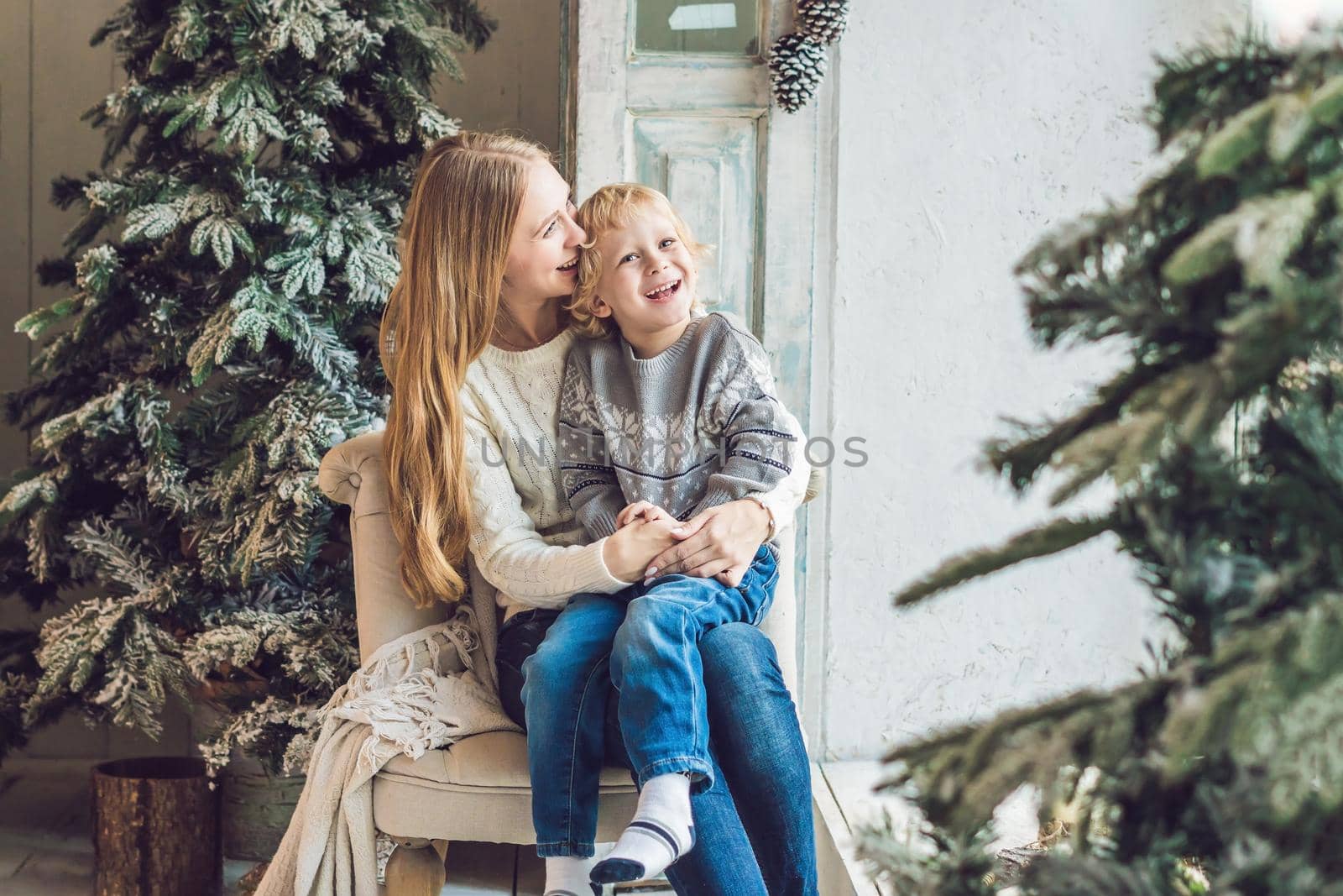 Portrait of happy mother and adorable boy celebrate Christmas. New Year's holidays. Toddler with mom in the festively decorated room with Christmas tree and decorations.