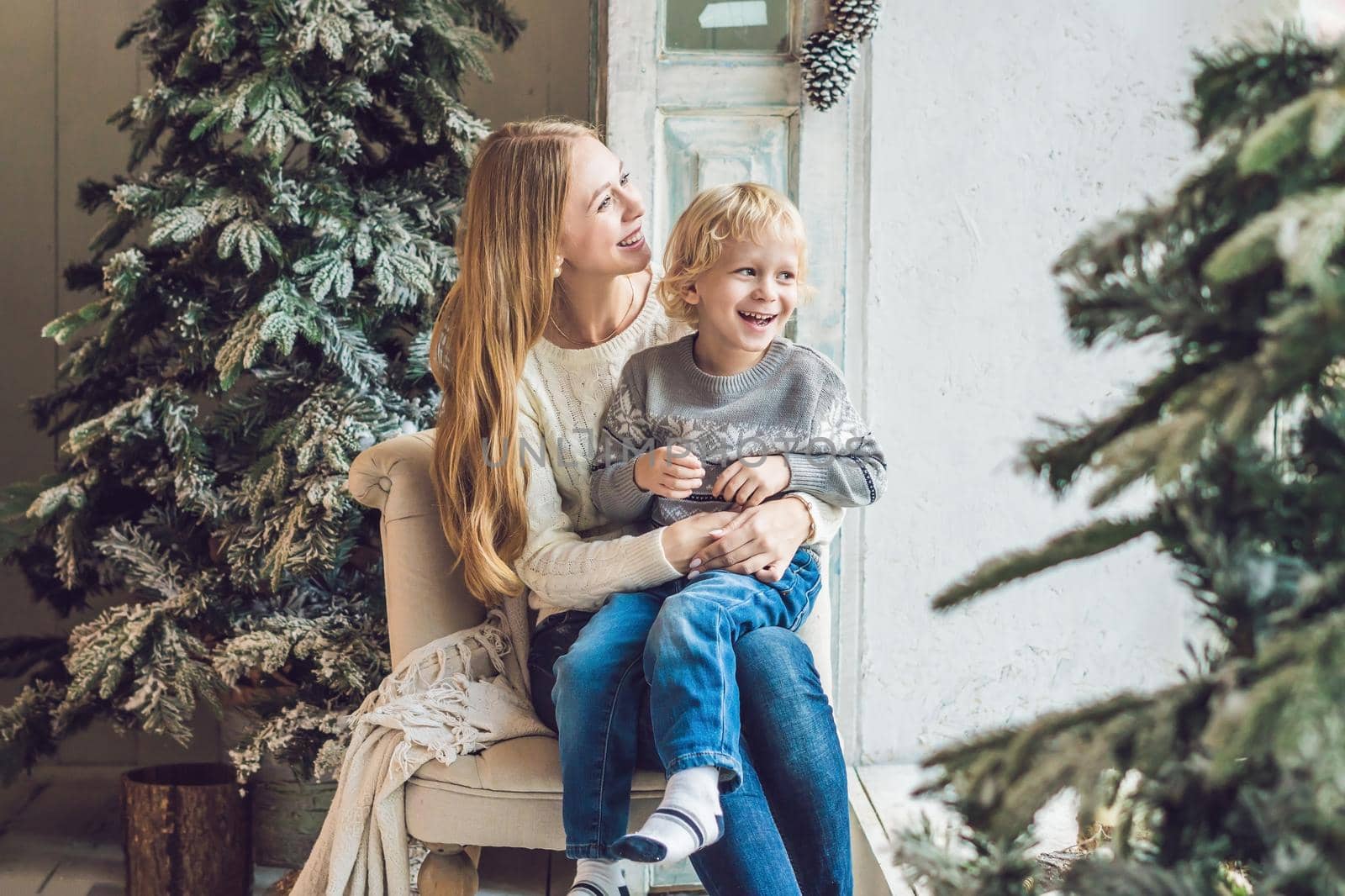 Portrait of happy mother and adorable boy celebrate Christmas. New Year's holidays. Toddler with mom in the festively decorated room with Christmas tree and decorations by galitskaya