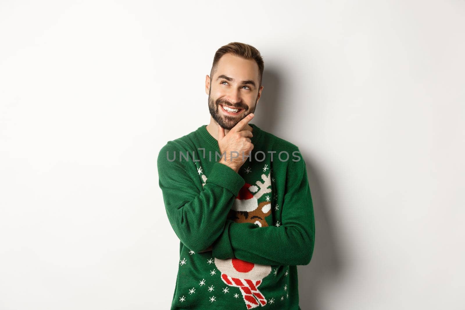 New year celebration and winter holidays concept. Thoughtful nice guy thinking about Christmas gifts, looking at upper left corner and smiling, white background by Benzoix