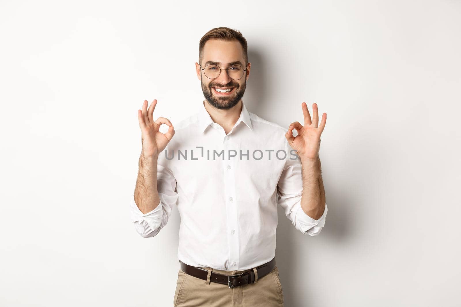 Satisfied handsome businessman showing ok sign, gurantee quallity, standing pleased against white background by Benzoix