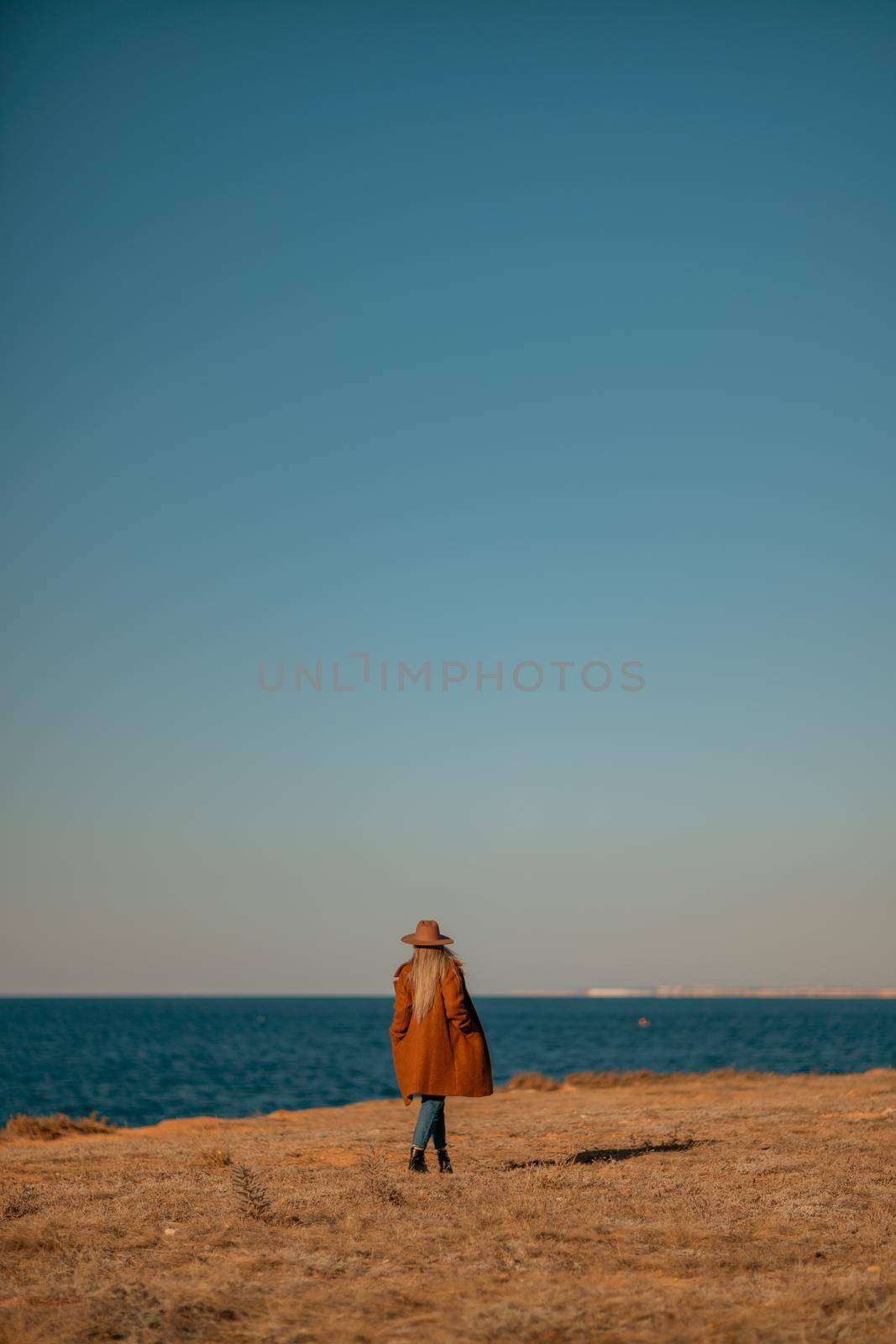 A woman walking along the coast near the sea. An elegant lady in a brown coat and a hat with fashionable makeup walks on the seashore.