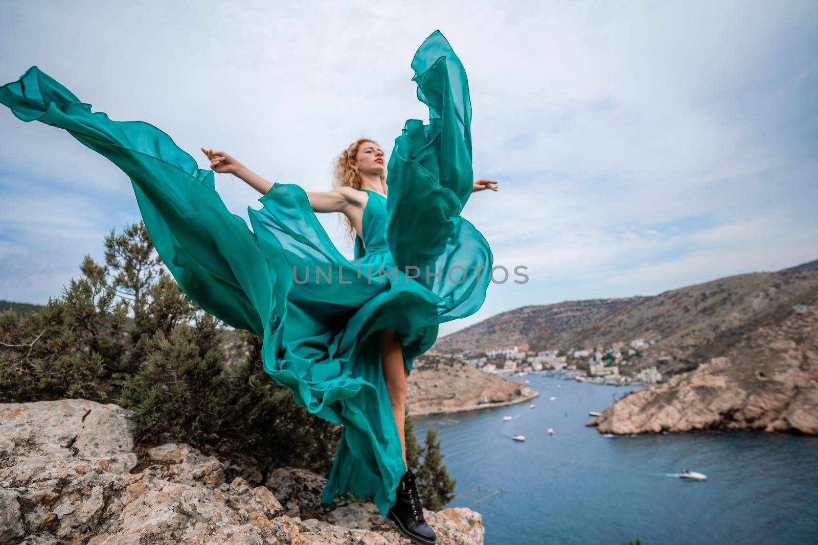 A woman in an emerald dress, a fashion model with long silk wings in a flowing dress, flying fabric on the embankment. by Matiunina